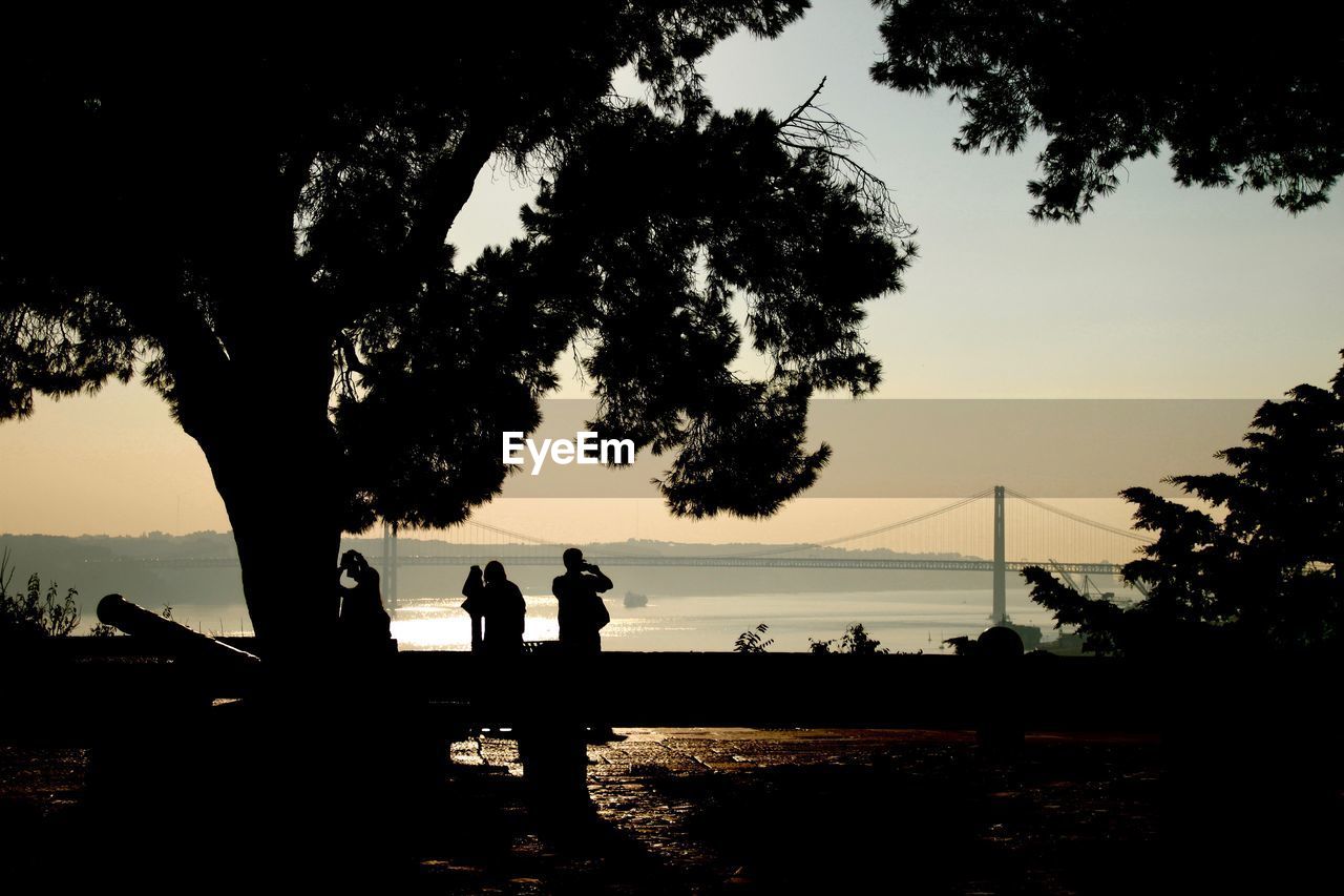 Silhouette people by river against sky during sunset