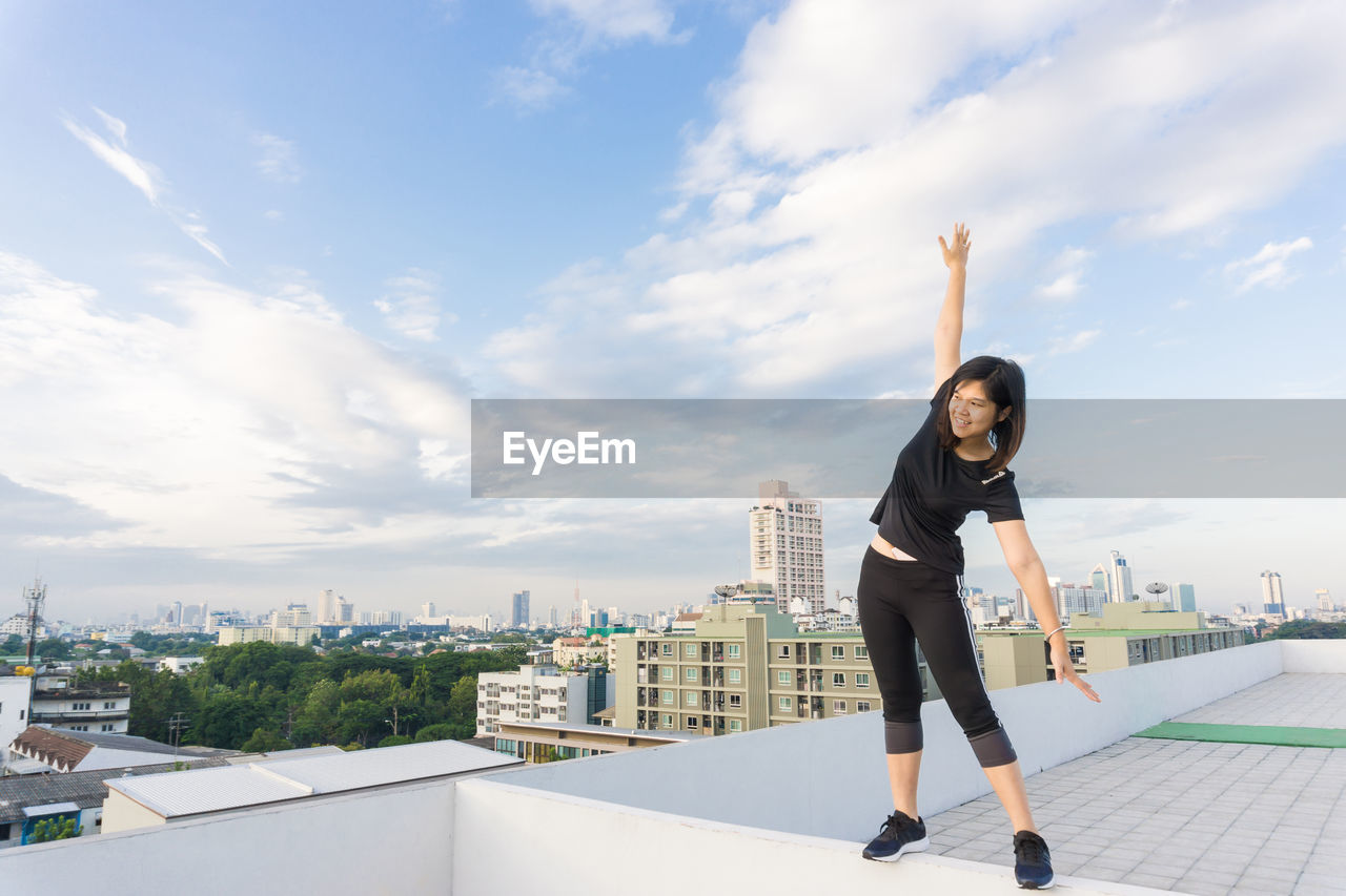 FULL LENGTH OF YOUNG WOMAN STANDING AGAINST SKY