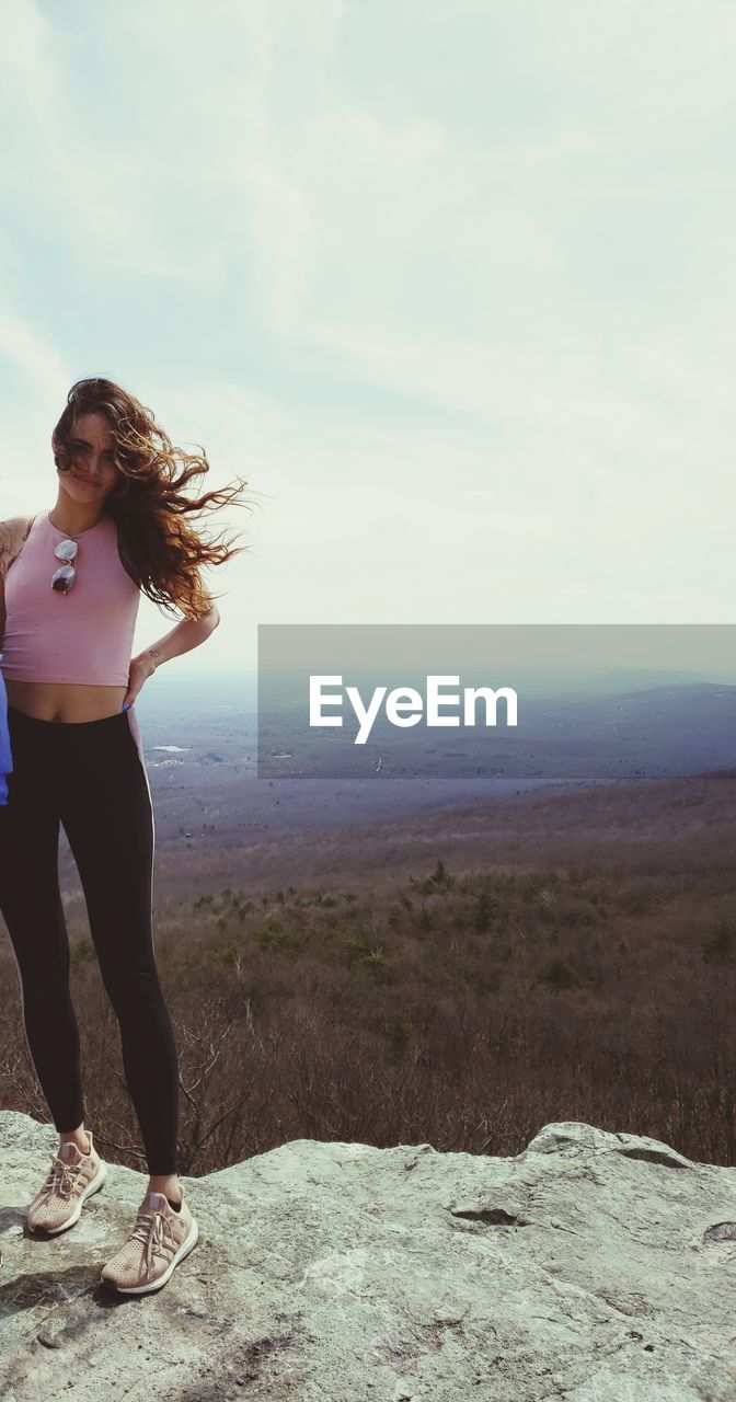 Full length of young woman standing on mountain against sky