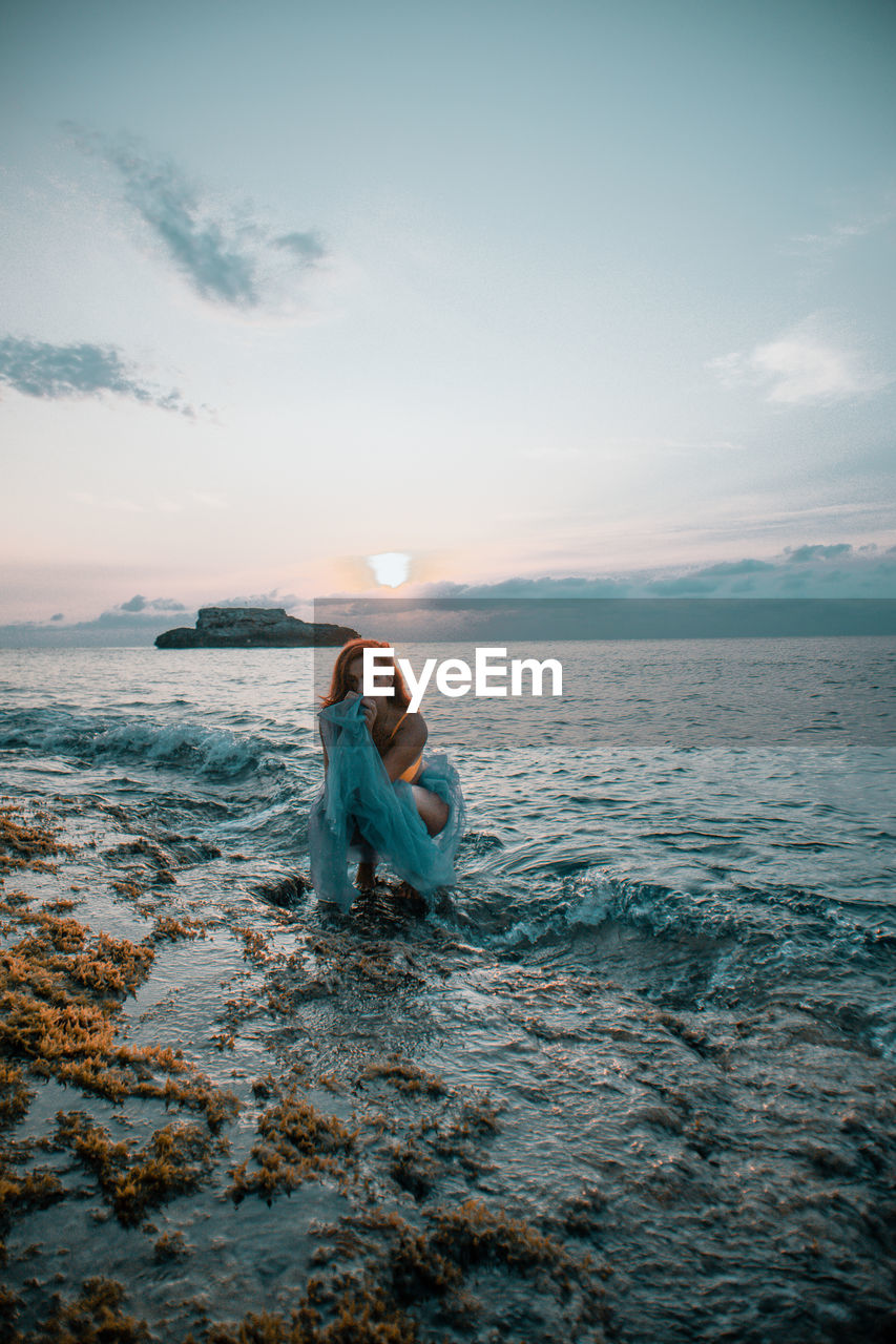 Woman in sea against sky during sunset