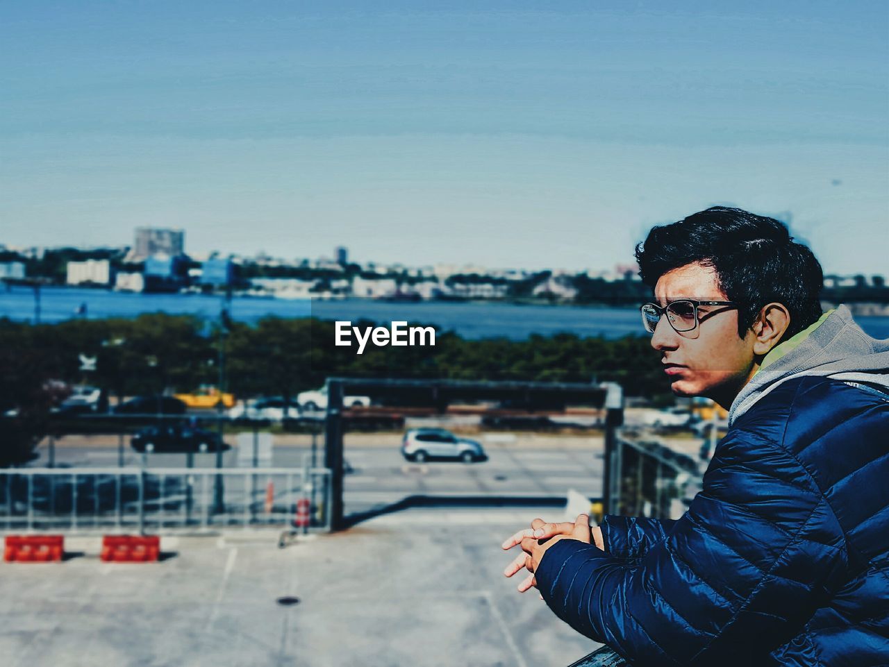 Side view of thoughtful young man against sky in city on sunny day