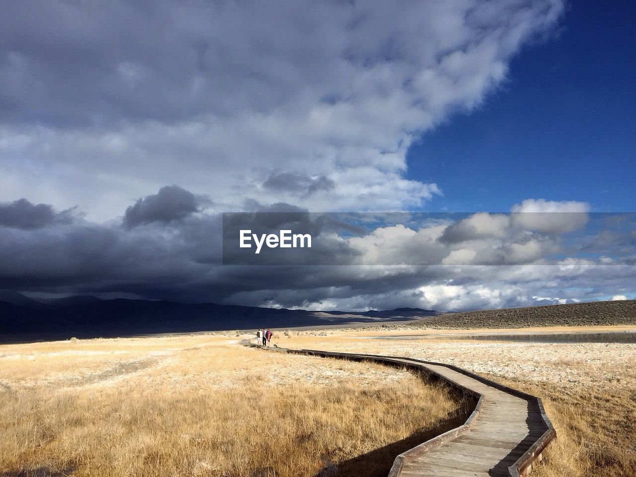 Friends walking on boardwalk against cloudy sky