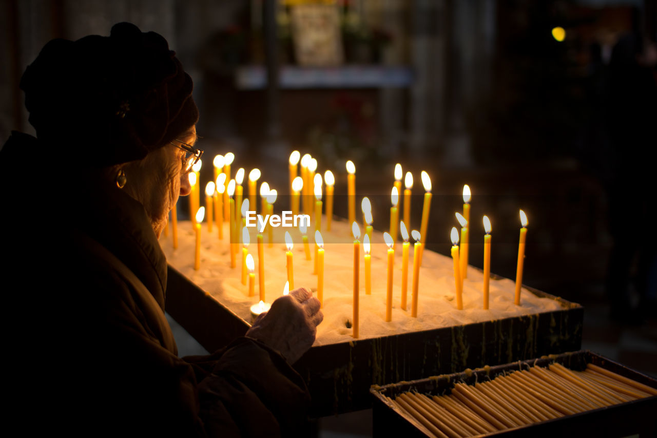 Side view of woman burning candles in church