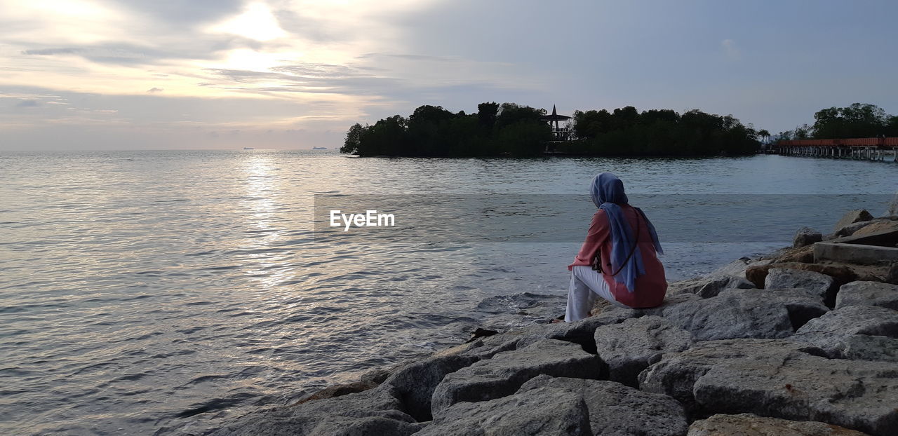 Rear view of woman sitting by sea on rock