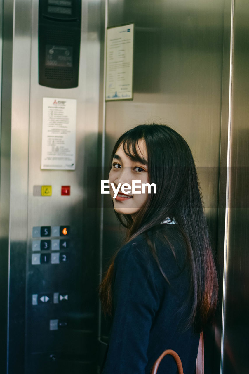 Portrait of young woman standing inside elevator in building