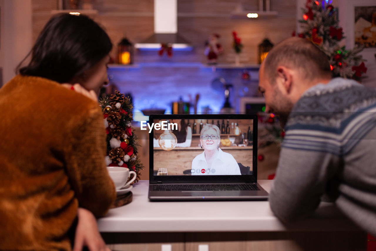 REAR VIEW OF MAN AND WOMAN USING SMART PHONE AT TABLE