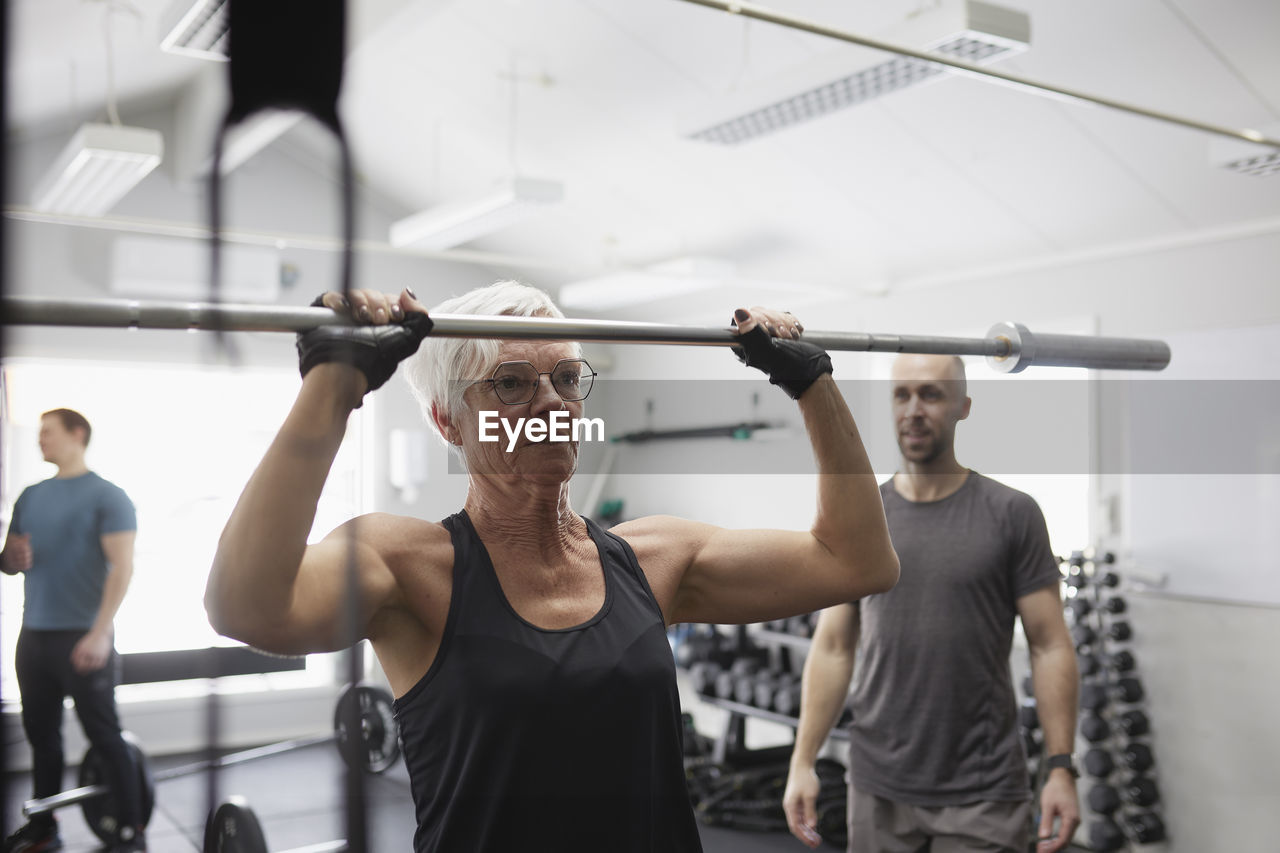 Senior woman lifting barbell pole in gym