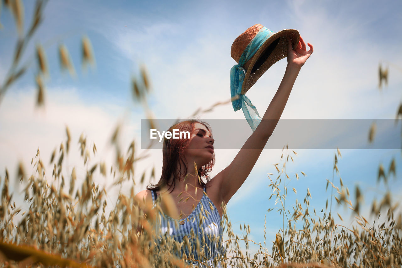 Woman with arms raised on field against sky