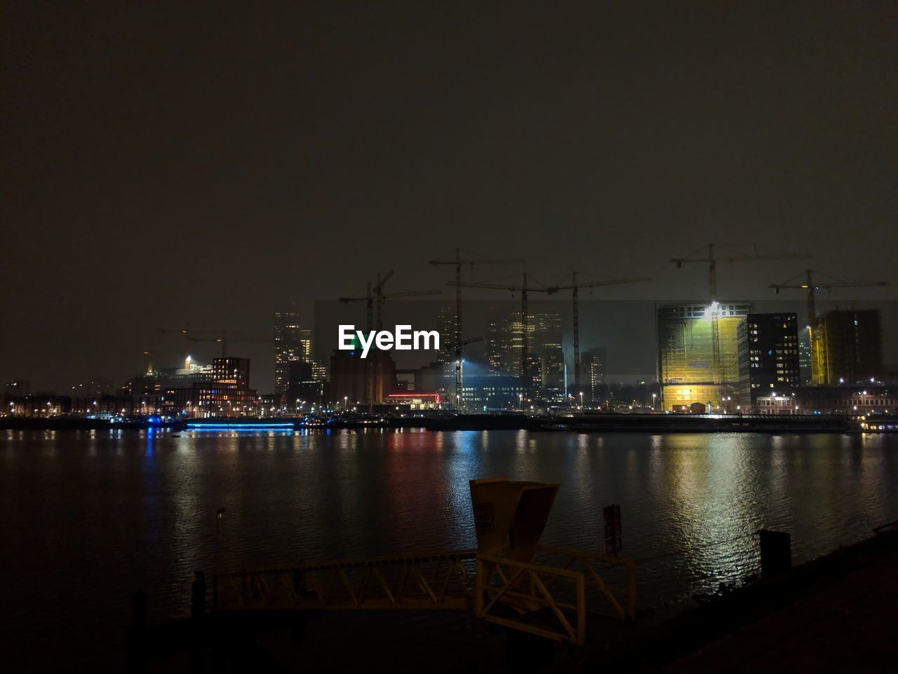 ILLUMINATED BUILDINGS BY RIVER AGAINST SKY