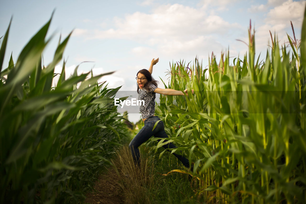 Surprised young woman amidst plants against sky on field