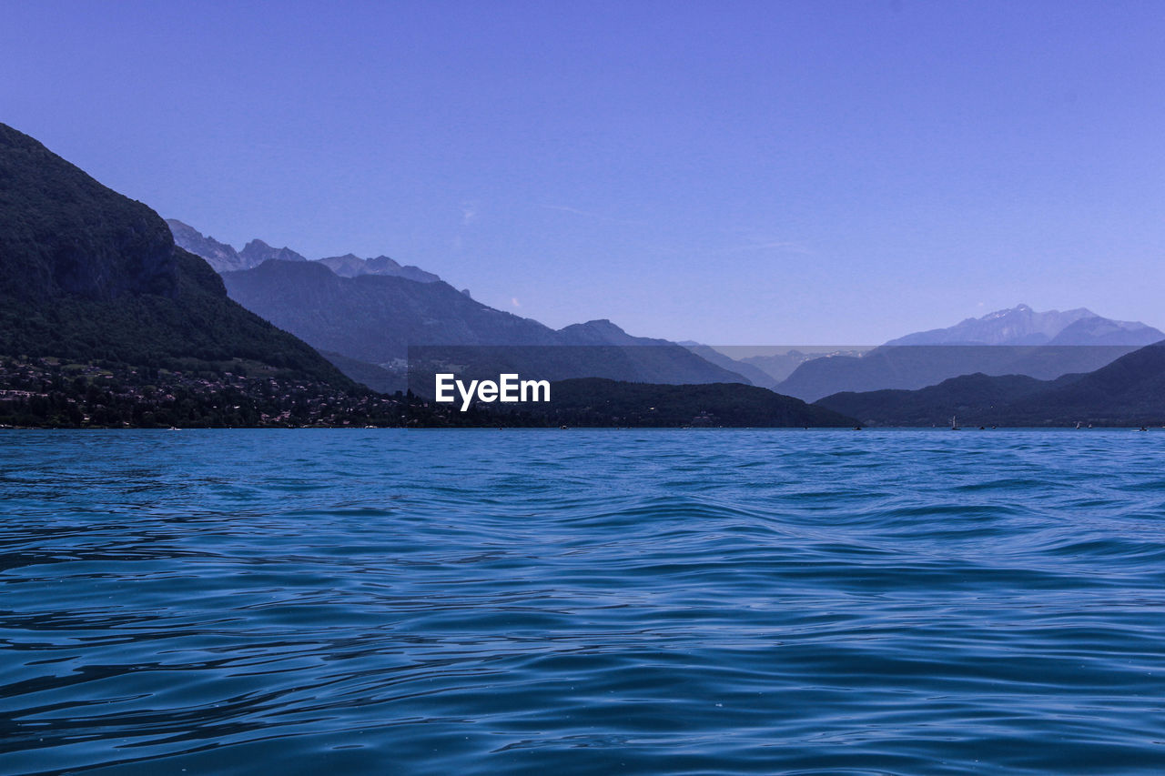 Scenic view of sea and mountains against clear blue sky