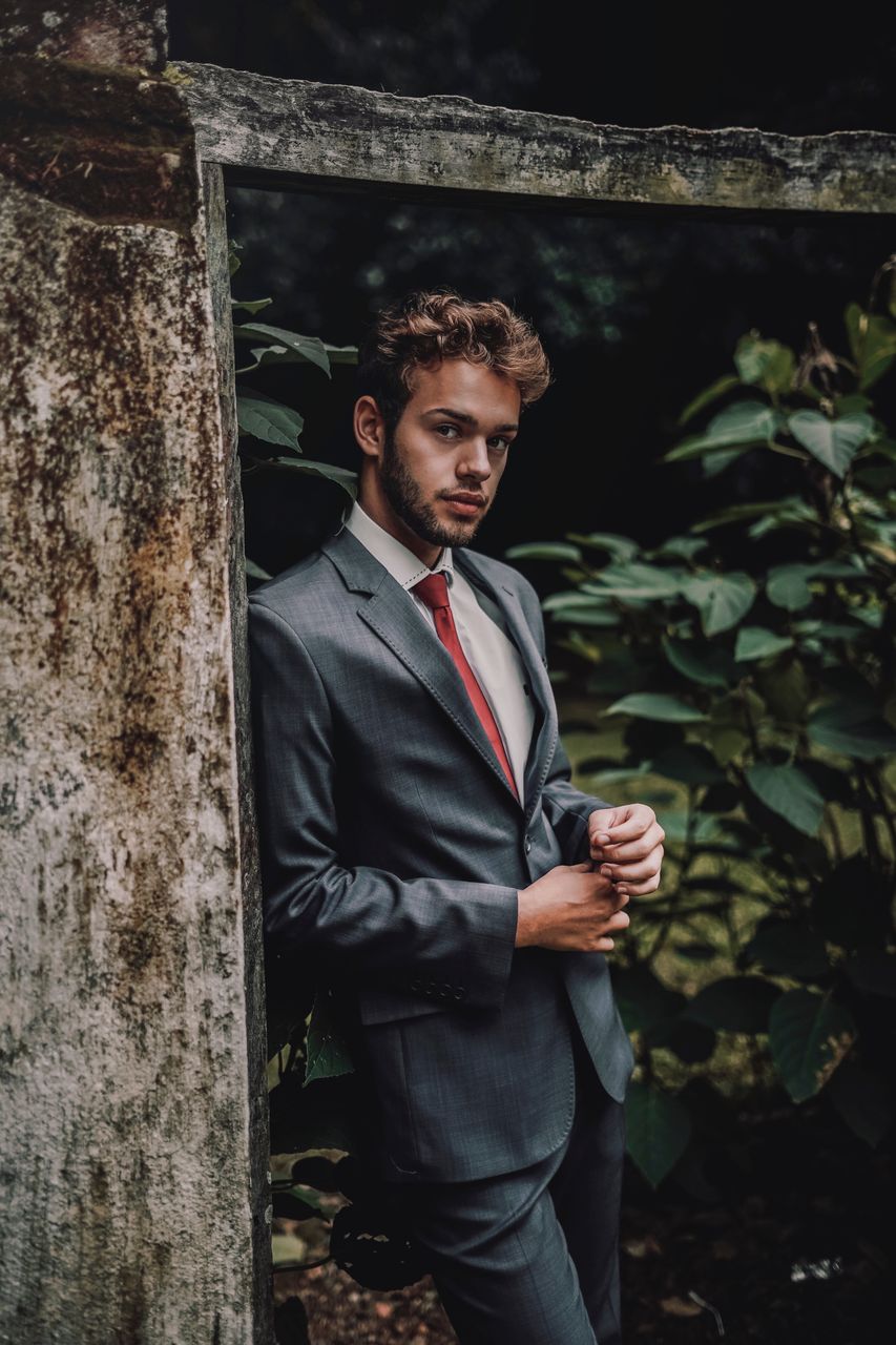 PORTRAIT OF YOUNG MAN STANDING AGAINST TREE