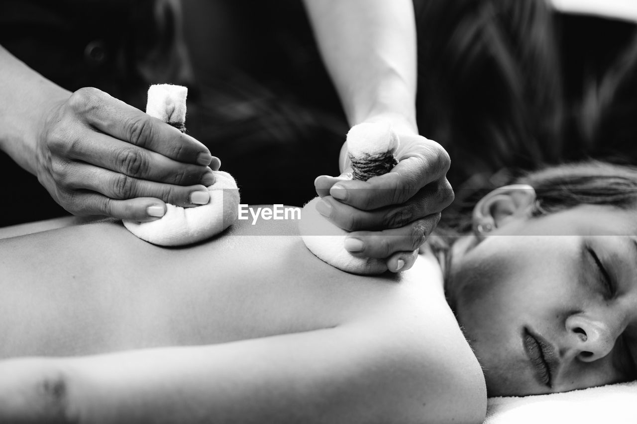 Hands of an ayurveda massage therapist pressing herbal bolus bags onto clients skin