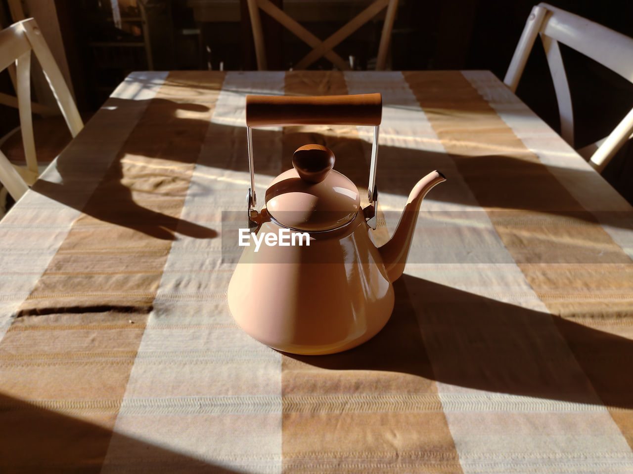 A cream colored teapot on the tablecloth in the morning time