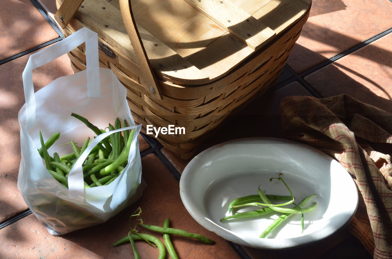 High angle view of green beans in bag by wicker basket on table