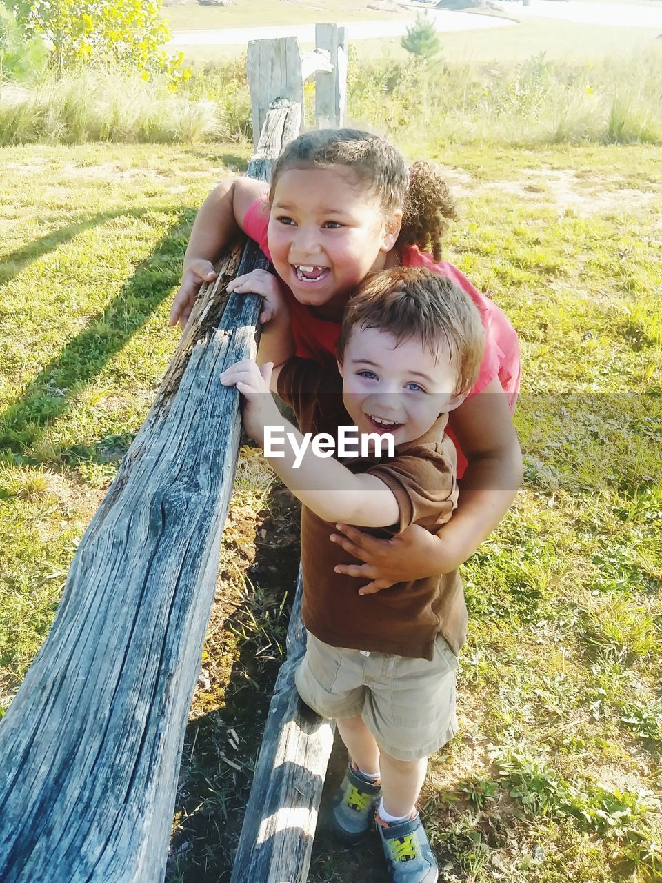 Happy siblings playing by wooden fence on grassy field
