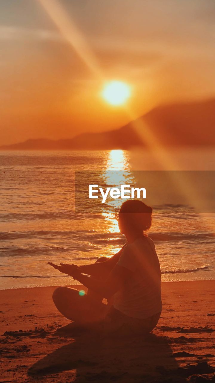 Rear view of woman sitting on beach during sunset