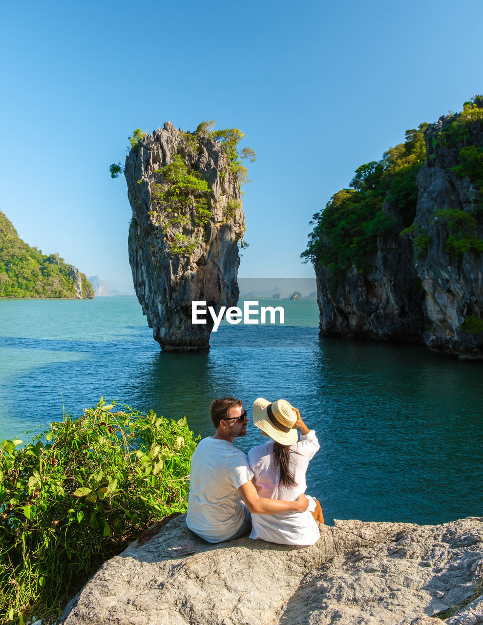 rear view of woman sitting on rock by sea against clear sky