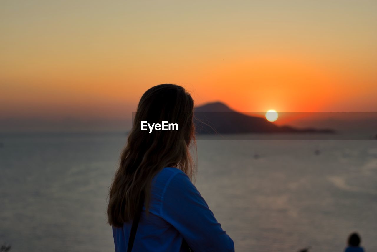 Side view of woman looking at sea against sky during sunset