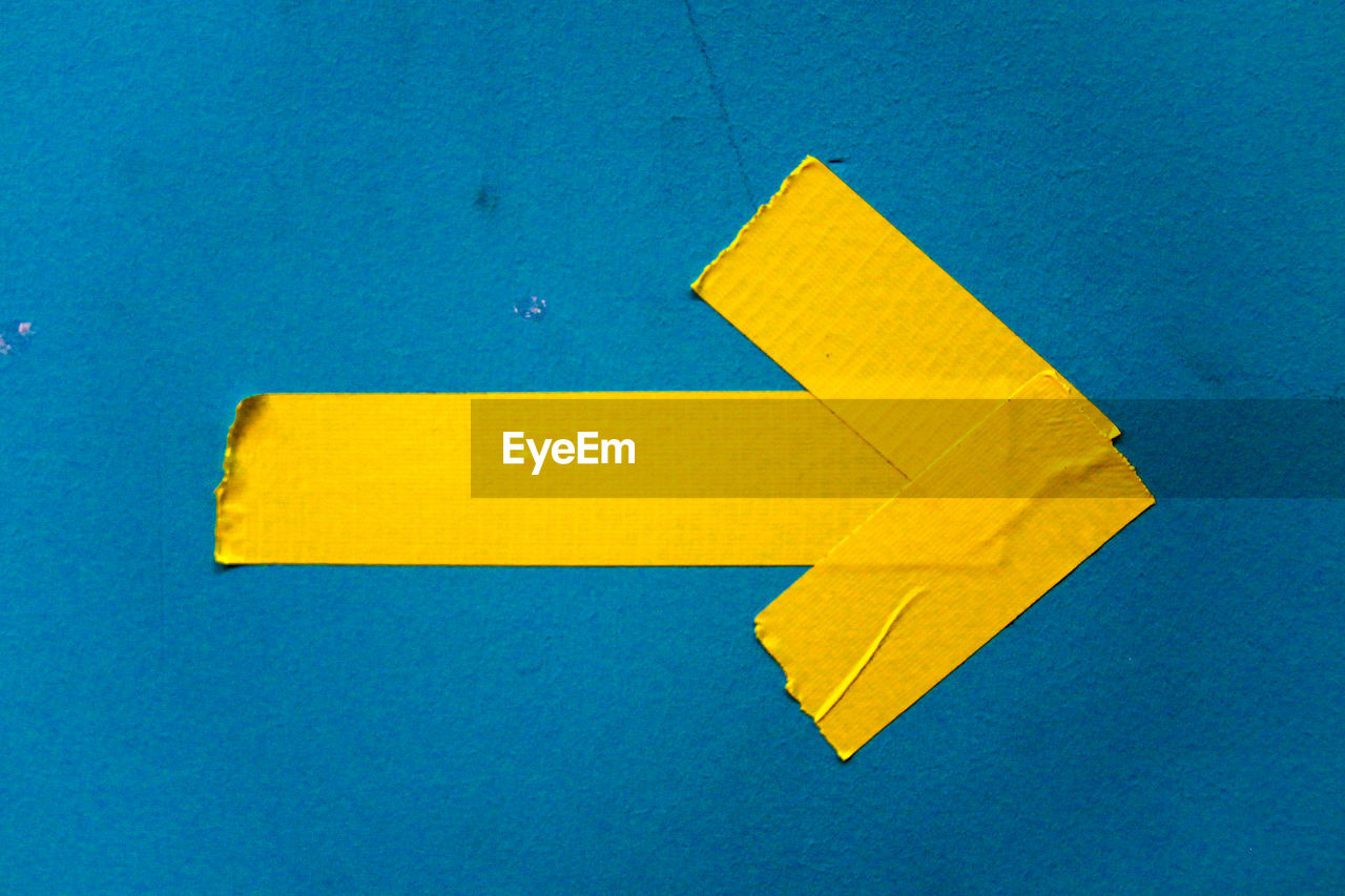 Close-up of yellow arrow symbol on blue wall
