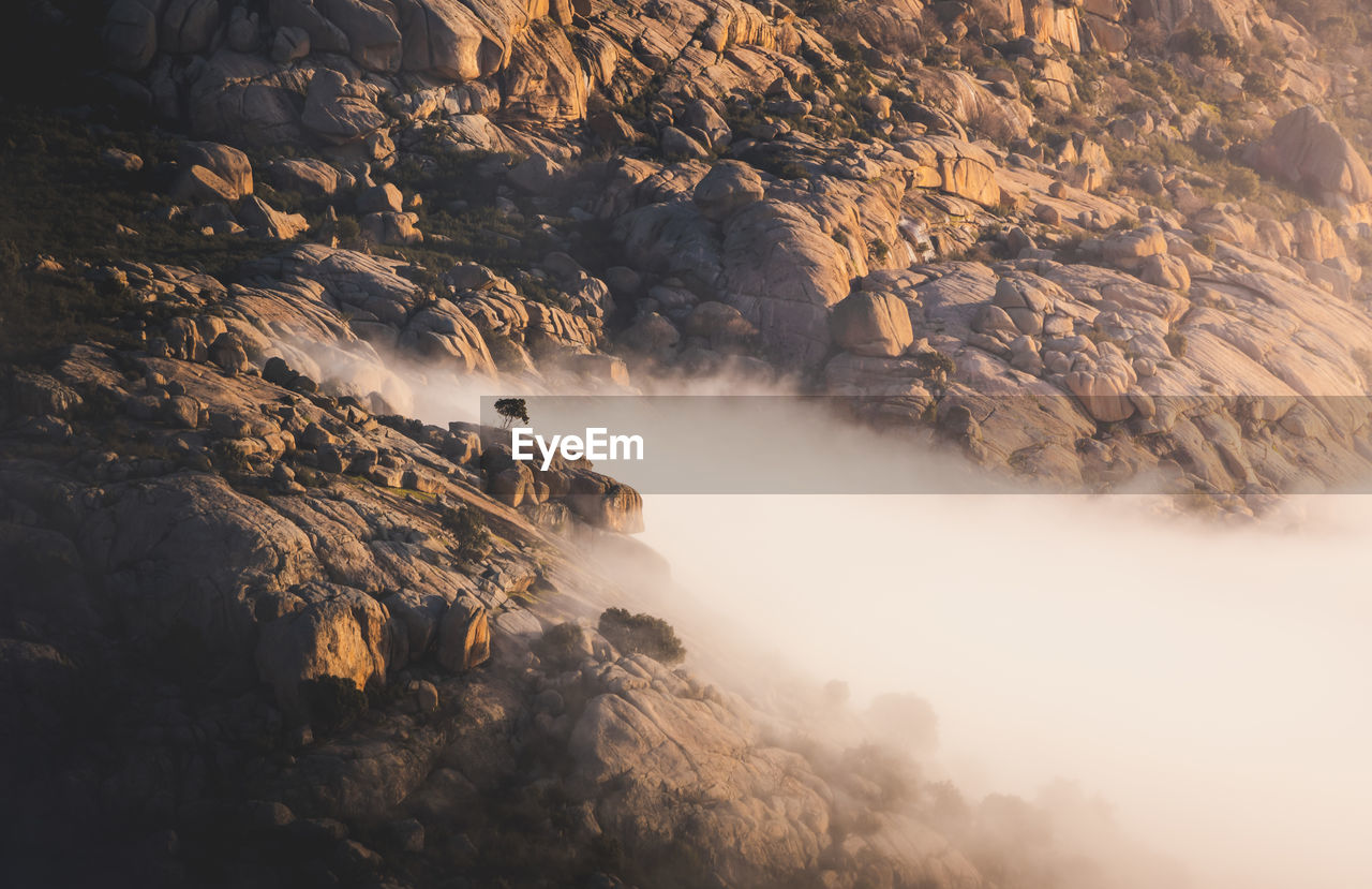 Scenic view of pedriza with mist diffusing between guadarrama mountain range and boulders with coniferous trees at sunrise in spain