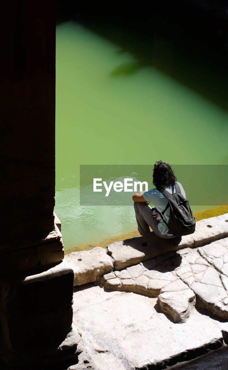 PERSON SITTING ON ROCK BY LAKE