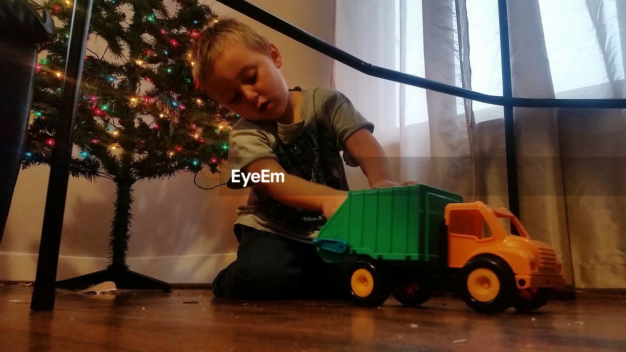 Boy playing with toy by christmas tree at home