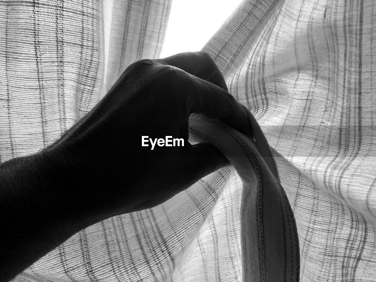 Cropped hand holding curtain at home