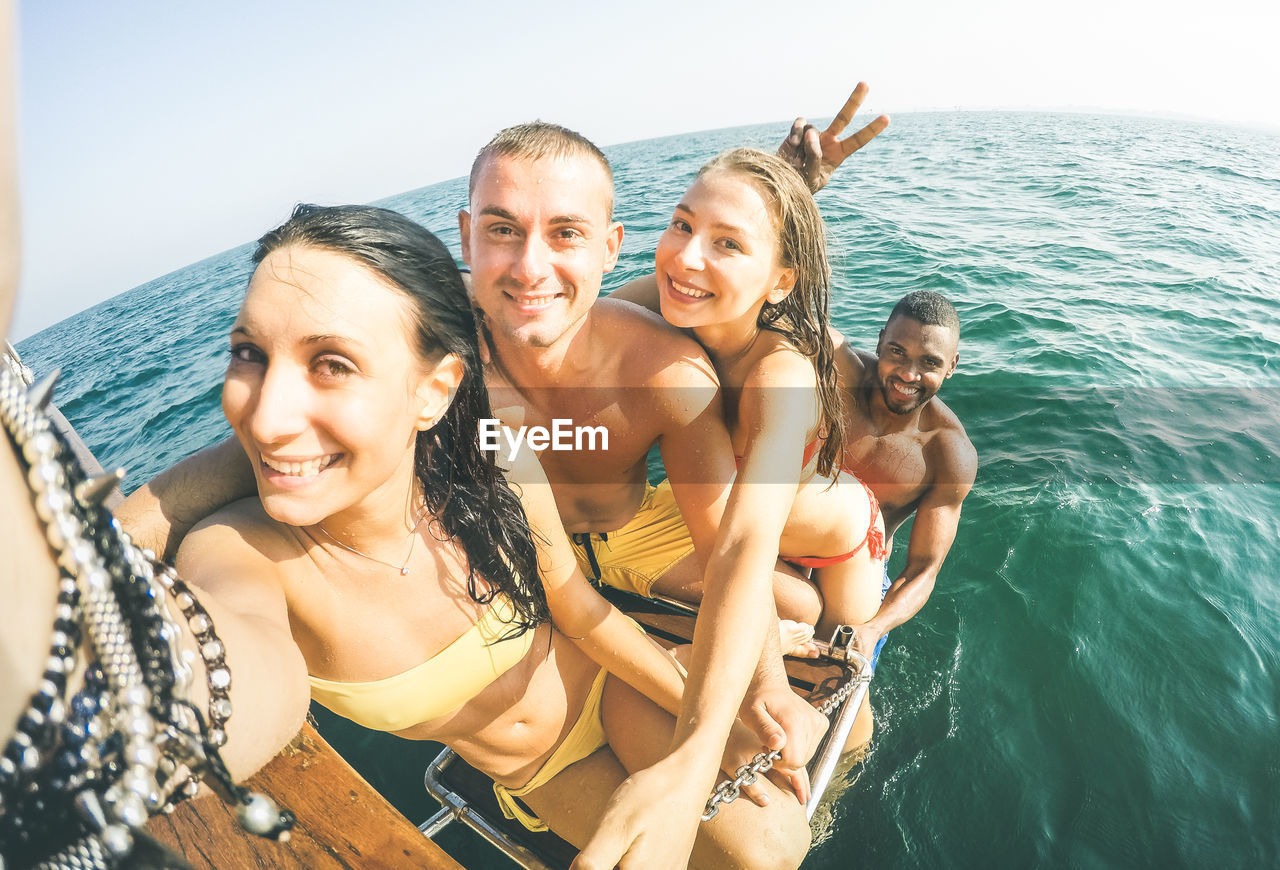 Fish-eye lens portrait of happy friends on boat ladder in sea