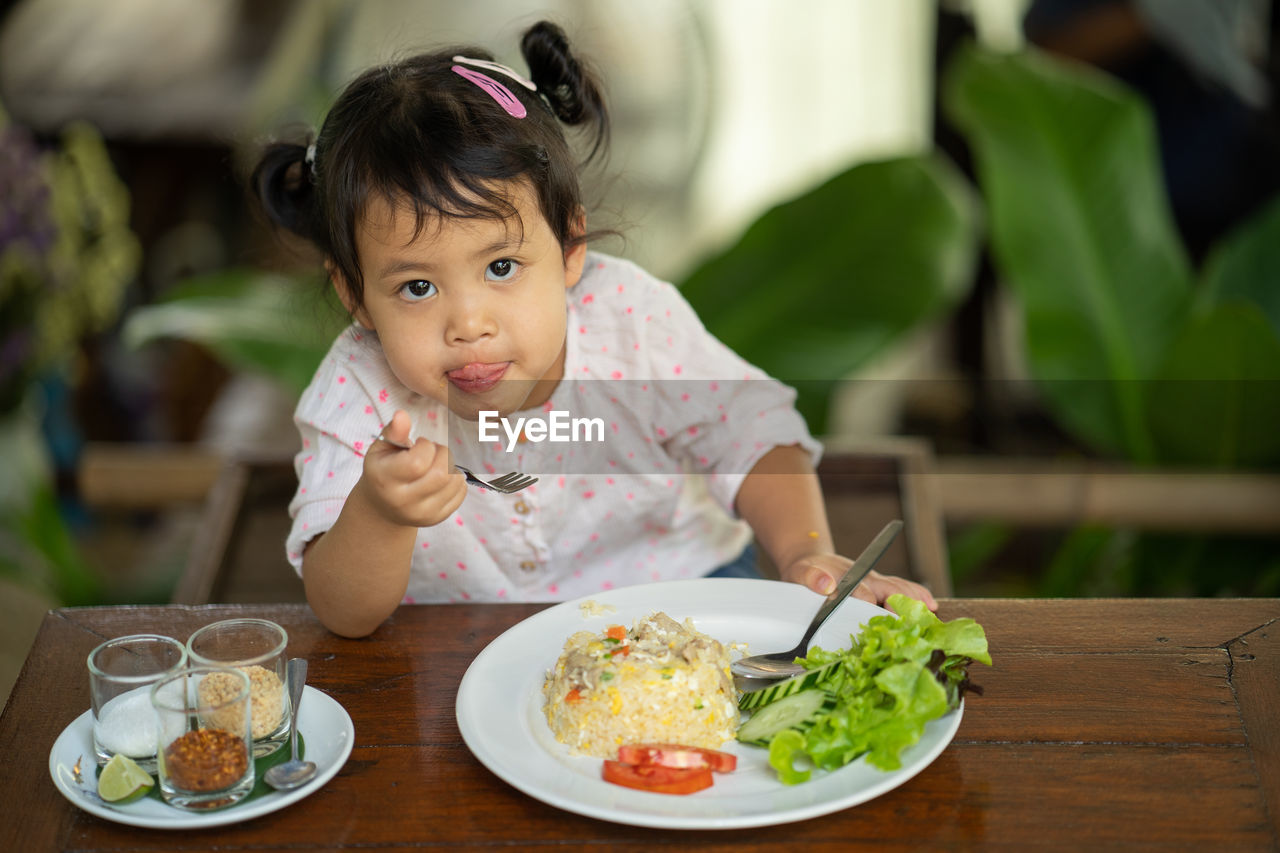 Cute little girl eating fried rice at wooden table.