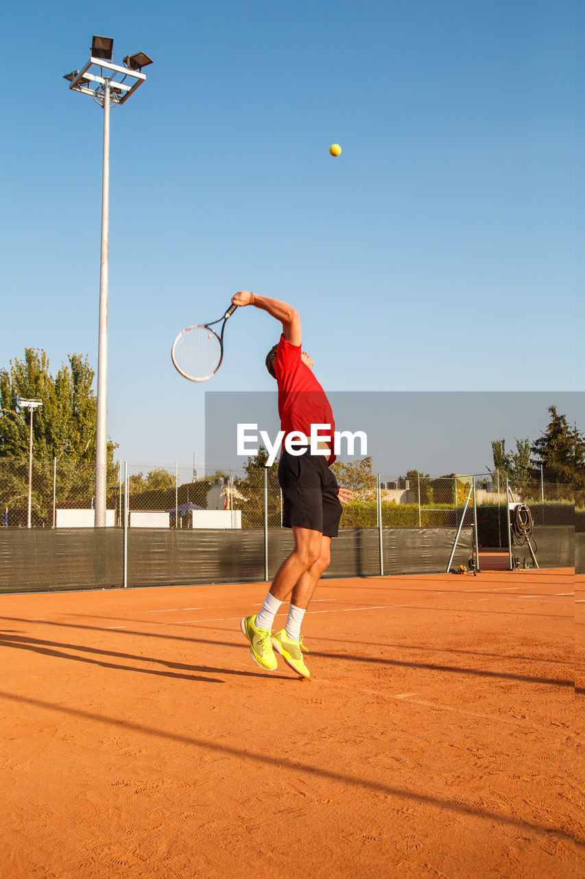 Man playing tennis on court against clear blue sky
