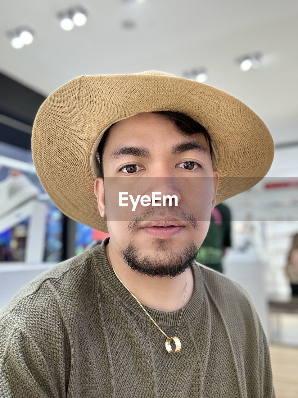 portrait, hat, one person, headshot, adult, clothing, looking at camera, facial hair, front view, sun hat, men, person, beard, indoors, focus on foreground, young adult, smiling, casual clothing, human hair, cowboy hat, hairstyle, emotion, human face, sombrero, close-up, happiness, standing, occupation