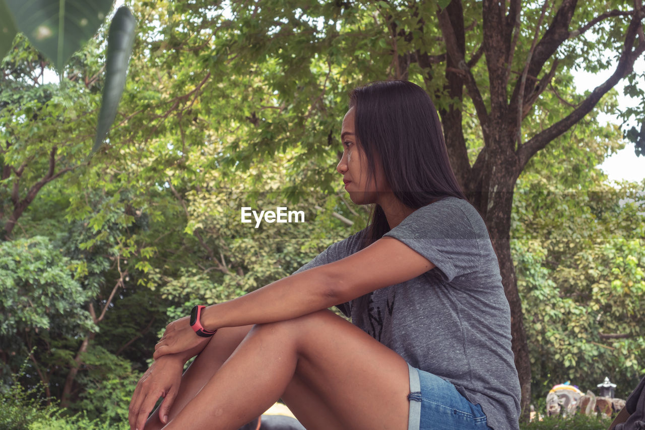 SIDE VIEW OF YOUNG WOMAN SITTING ON PLANT