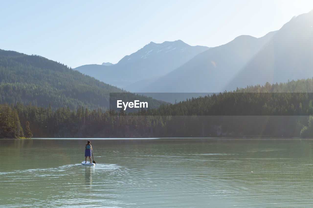 Pregnant woman paddleboarding on peaceful mountain lake