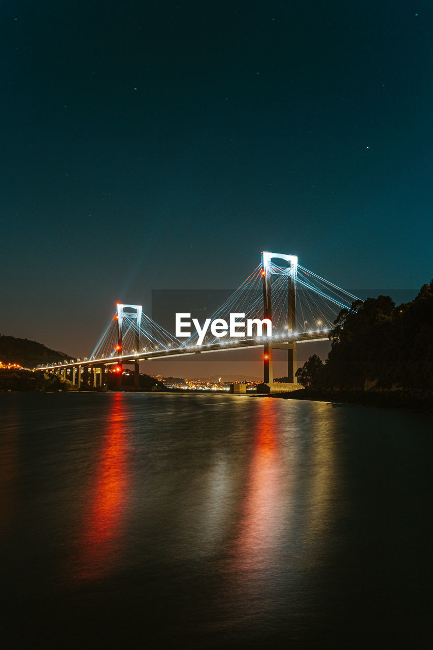 Illuminated bridge over river at night