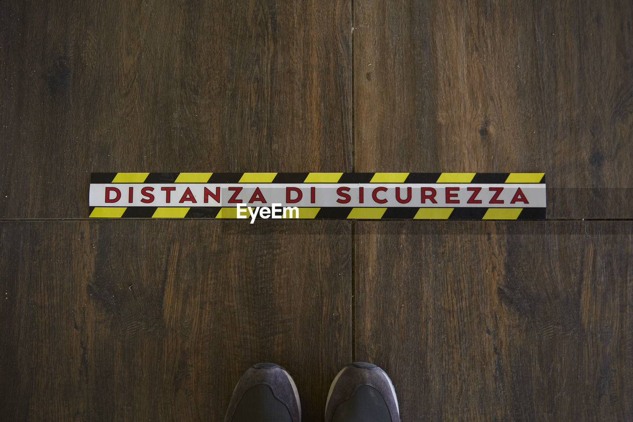 LOW SECTION OF PERSON STANDING BY TEXT ON WOODEN SIGN