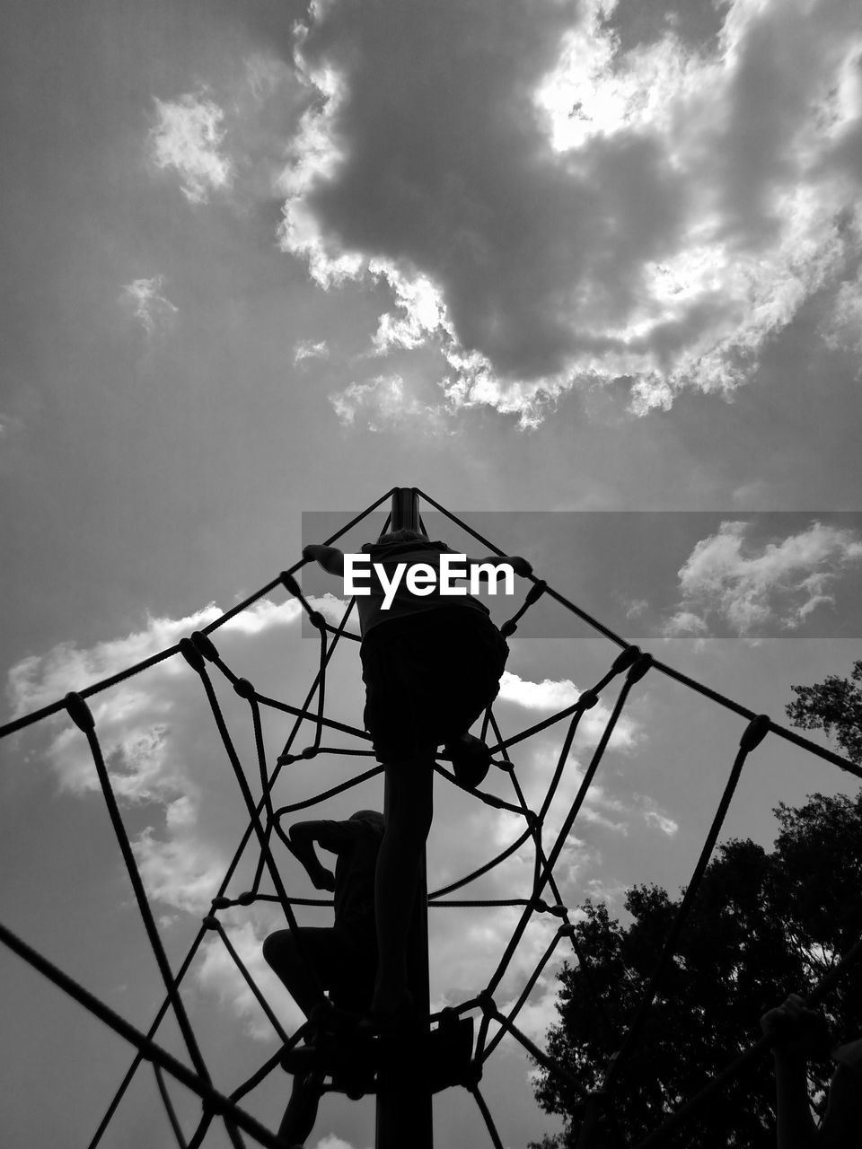 Low angle view of silhouette children climbing jungle gym against sky at playground