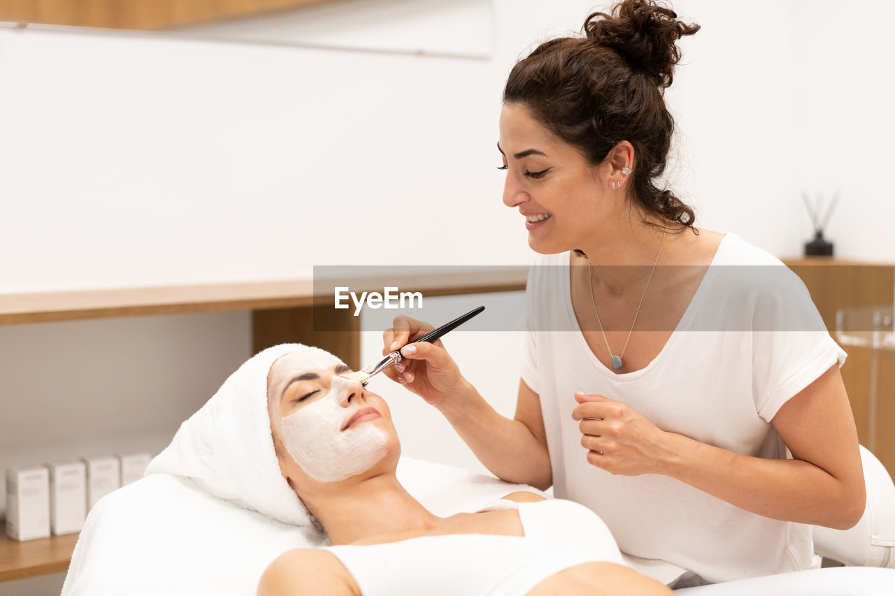 side view of young woman applying make-up to daughter at home