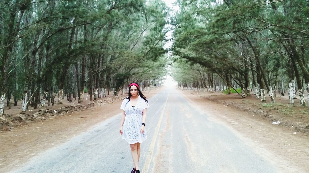 Woman walking on country road along trees