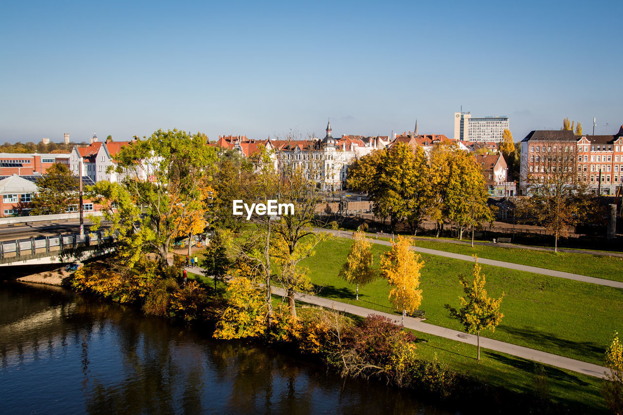 PLANTS AND TREES BY RIVER AGAINST BUILDINGS IN CITY