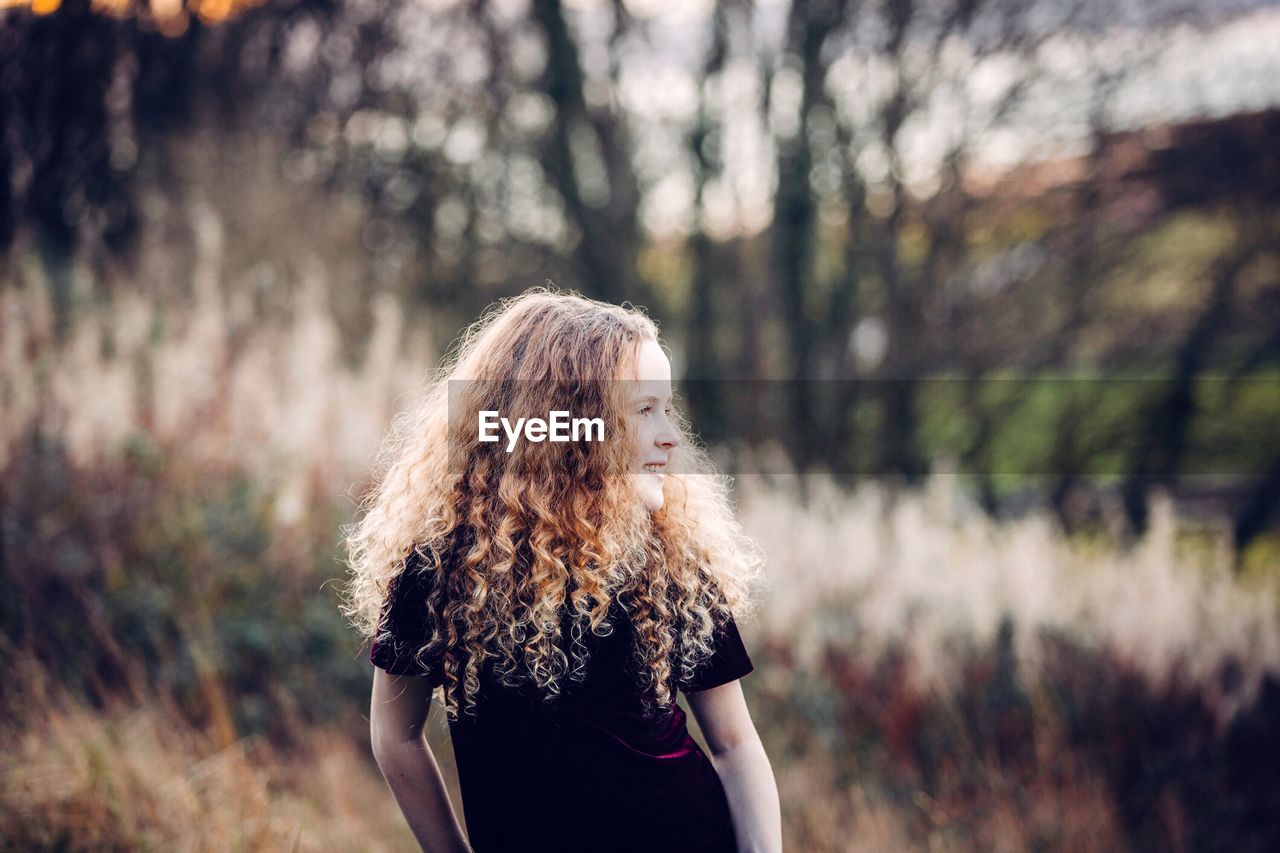 Cute girl looking away while standing against trees in forest