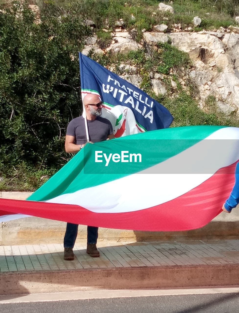 REAR VIEW OF MAN HOLDING FLAG AGAINST BLUE UMBRELLA