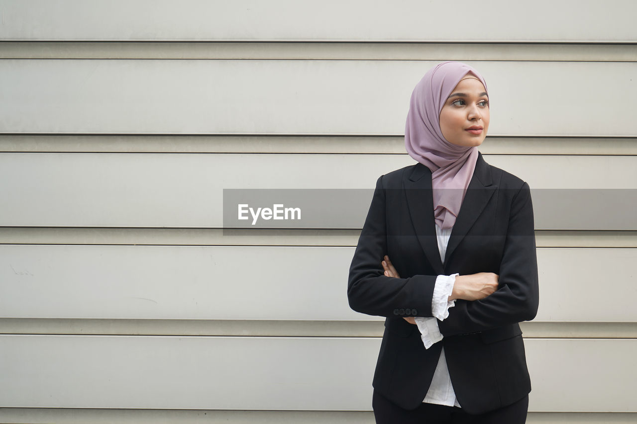 PORTRAIT OF A YOUNG WOMAN STANDING AGAINST WALL