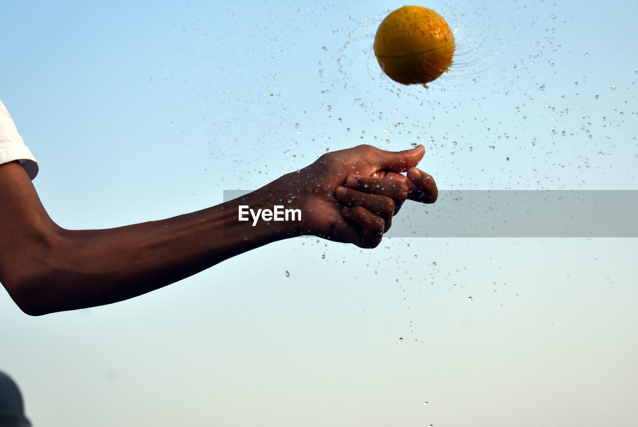 Skinny man hand spinning the wet watery ball in air with sky blue background 