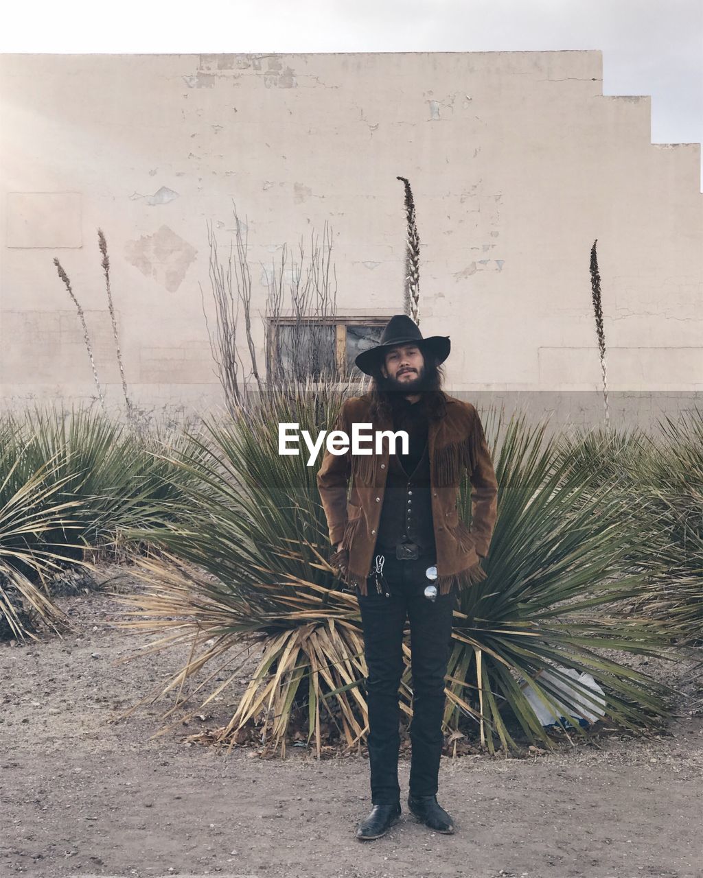 Portrait of cowboy standing by plant against wall