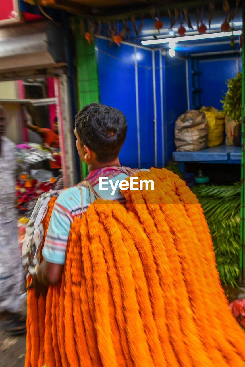 REAR VIEW OF MAN STANDING AT MARKET