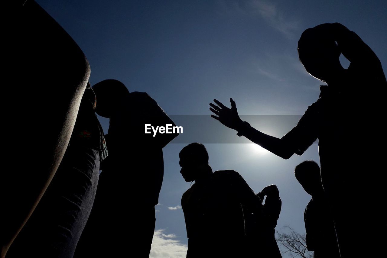 Low angle silhouette people standing against sky during sunset