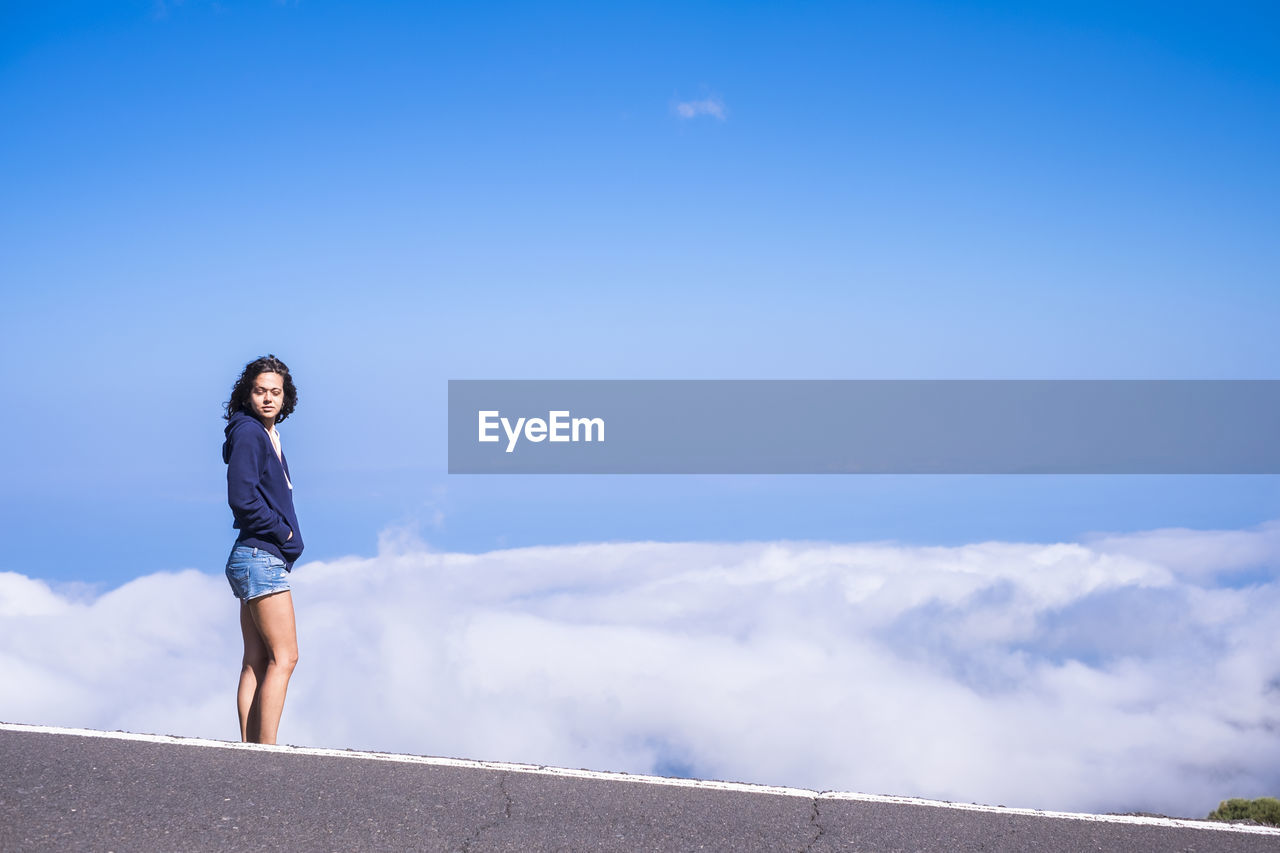 Side view of woman standing on road against sky during sunny day