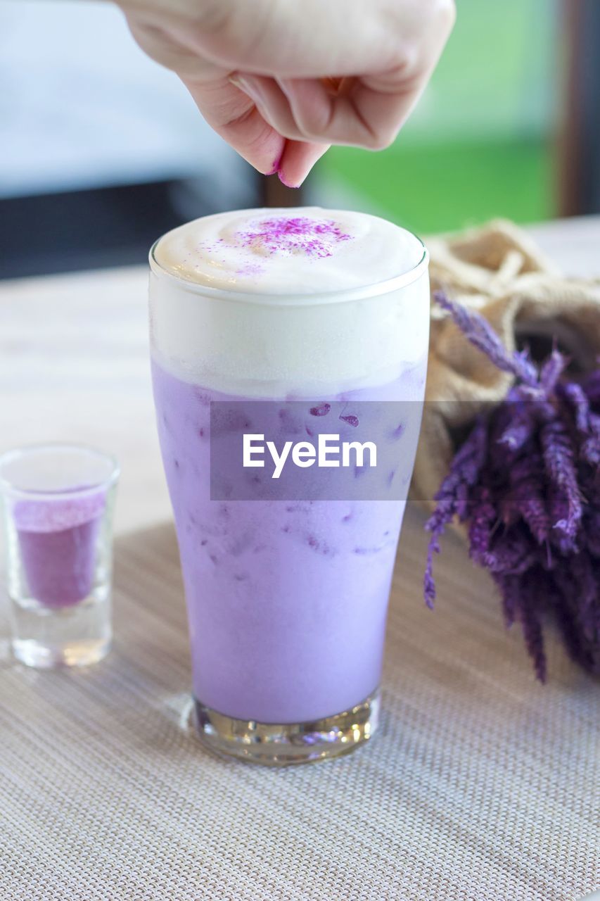 Cropped hand sprinkling ingredient in purple drink on table