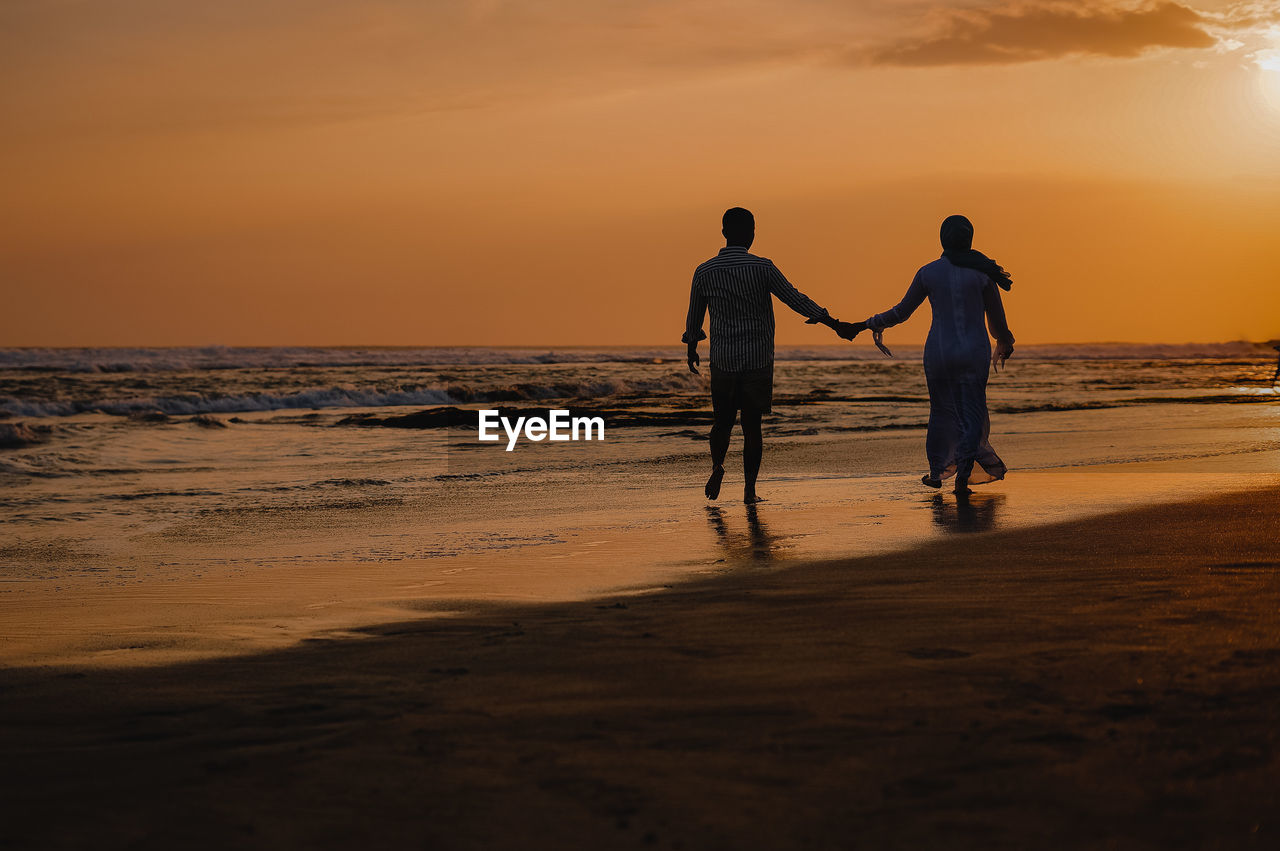 Full length of friends on beach against sky during sunset